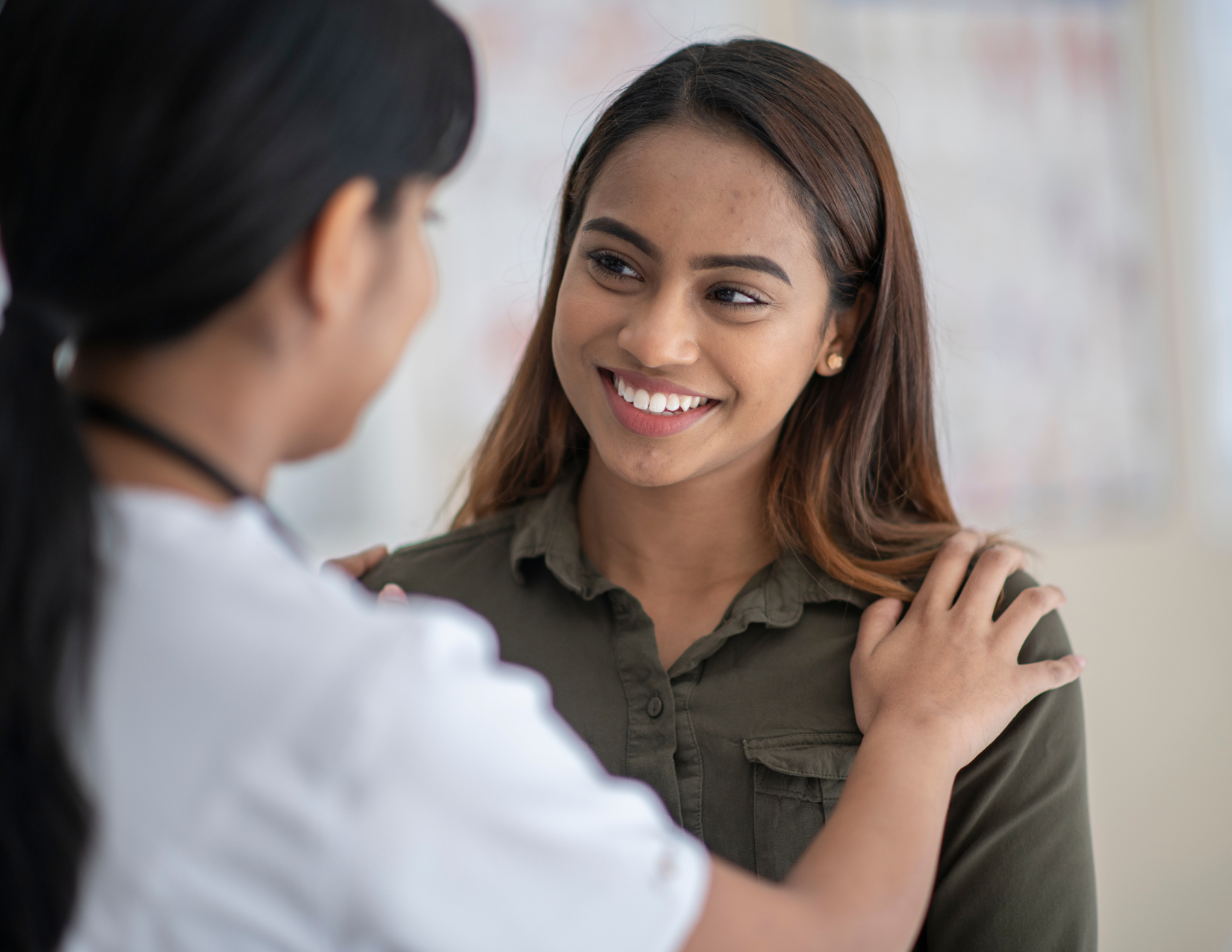 A young woman smiling at another woman who has her hand on her shoulder 